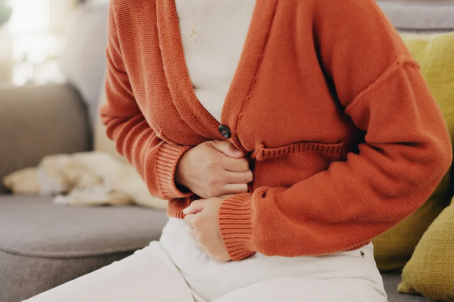 A person holding their lower abdomen while seated, illustrating pelvic pain commonly associated with PCOS or PMOSer abdomen, suggesting pelvic or abdominal discomfort