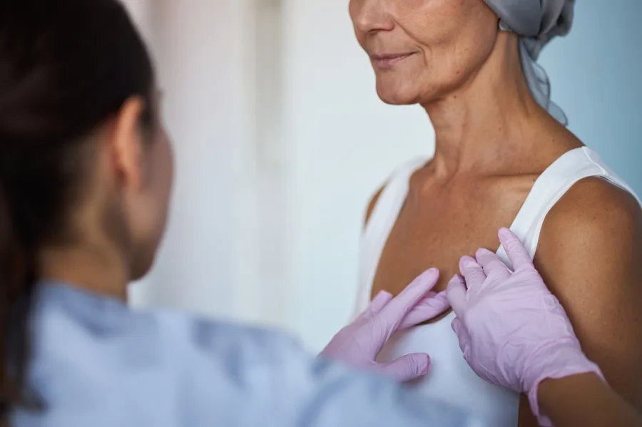 Breast cancer nurse navigator performing a gentle chest exam on a patient, offering supportive, personalized care.