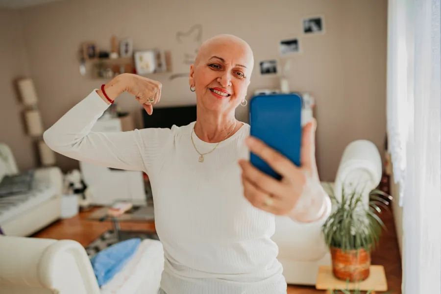 A woman flexing her arm and smiling while taking a selfie, conveying strength after breast cancer surgery.