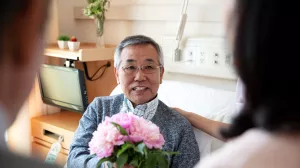 Senior inpatient sits up and cheers up in hospital bed after receiving donated flowers.