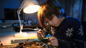 Child is playing and fixing an electronic device at their desk and using a desk light.