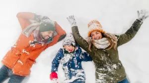 Two adults and child laying in the snow in winter clothes