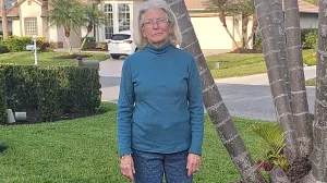 Woman in teal colored sweater stands outside.