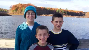 Three children stand by a lake on a Fall day