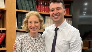 Two people standing with a bookshelf behind them.