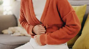 A person holding their lower abdomen while seated, illustrating pelvic pain commonly associated with PCOS or PMOSer abdomen, suggesting pelvic or abdominal discomfort