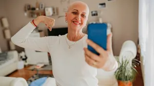 A woman flexing her arm and smiling while taking a selfie, conveying strength after breast cancer surgery.