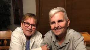 Man and woman sit around cake that says "Happy 50th Anniversary"