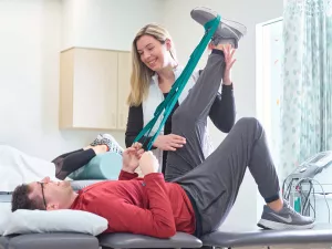 Physical Therapist, Courtney Bua, helping a rehabilitation patient stretch leg using a resistance band.