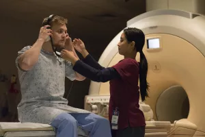 MRI radiation technologist prepping and helping patient put on headphones before MRI scan at Tufts Medical Center.