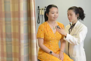 Jenny Ruan, MD checking patient's heart with a stethoscope during an appointment at Tufts Medical Center's OBGYN Asian Access Clinic.