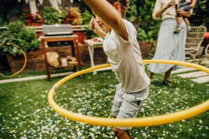 Child swinging a hula hoop around hips during a backyard birthday party.