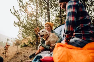 Couple camping with their dog in autumn and sitting outside of their tents.