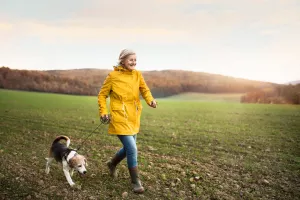 Senior wearing a raincoat running through a field with dog during autumn.