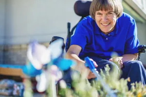 Multiple sclerosis patient in a wheelchair watering plants outside of home.