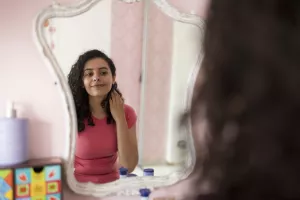 Teen looking at their reflection in their bedroom mirror.
