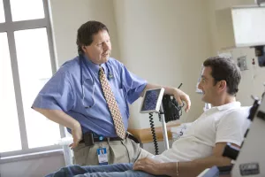 Ray Comenzo, MD (Director of Blood Bank, Transfusion and Stem Cell Services at Tufts Medical Center) talking to and examining patient during an appointment with aphoresis equipment.