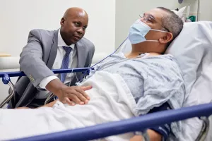 Dr. Jason Hall, Surgeon-in-Chief and Chair of the Department of Surgery at Tufts Medical Center, talking to patient before surgery and placing his hand on patient's stomach for exam.