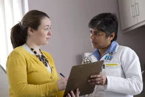 Neuro-oncologist Suriya Jeyapalan, MD, MPH is talking to a patient about paperwork on a clipboard in clinic appointment at Tufts Medical Center's Cancer Center.