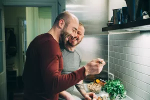 LGBTQ couple cooking in home kitchen and laughing.