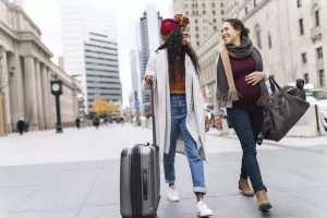 LGBTQ couple walking on a city sidewalk and smiling with their luggage.