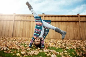 Child laughing and doing a cartwheel in their backyard during autumn with fallen leaves.