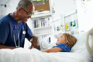 Nurse talking and laughing with pediatric inpatient lying in hospital bed.