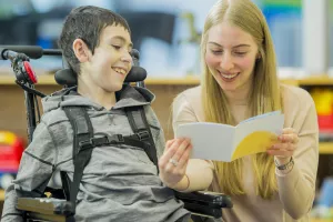 Specialist reading to a pediatric complex care patient who has a disability and is sitting in a wheelchair.