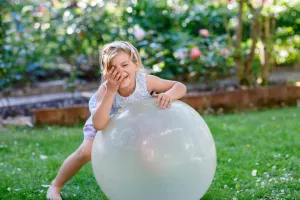 Child playing in backyard with a giant exercise ball and laughing.