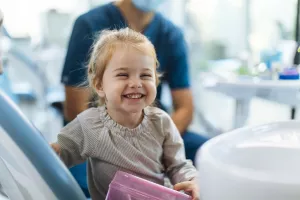 Toddler smiling in dentist chair after dental exam appointment.