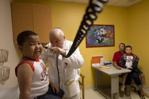  Lawrence S. Milner, MD, Chief of Pediatric Nephrology, examines 5-year-old patient's ear in a clinic appointment while family looks on.