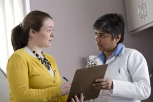Neuro-oncologist talking to a patient about paperwork on a clipboard in clinic appointment at Tufts Medical Center's Cancer Center.