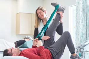 Physical Therapist, Courtney Bua, helping a rehabilitation patient stretch leg using a resistance band.