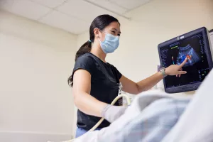 Kim-Yen Vo, Ultrasound Technologist, pointing at computer screen and talking to patient while performing ultrasound at MelroseWakefield Hospital.