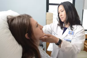 Patient's face is being examined for skin cancer in the dermatology clinic at Tufts Medical Center by Clarissa Yang, MD.