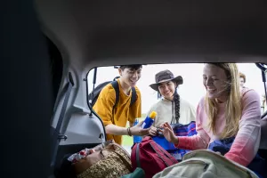 Friends wearing sun protection (long shirts, hats and sunscreen) are gathering their items from the back of their roadtrip car.