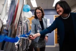 Two researchers cutting a ribbon to a balloon