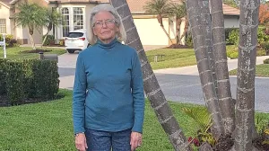 Woman in teal colored sweater stands outside.
