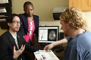 Lester Leung, MD, Director, Comprehensive Stroke Center at Tufts Medical Center; Director, Stroke and Young Adults (SAYA) Program, and Adedayu Dansu, Stroke Coordinator, adult neurology, discussing brain scans, condition with patient.