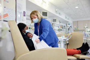 Debra Call, RN covering a mother and her newborn with a blanket while they lay back in a lounge chair in the special care nursery at MelroseWakefield Hospital.